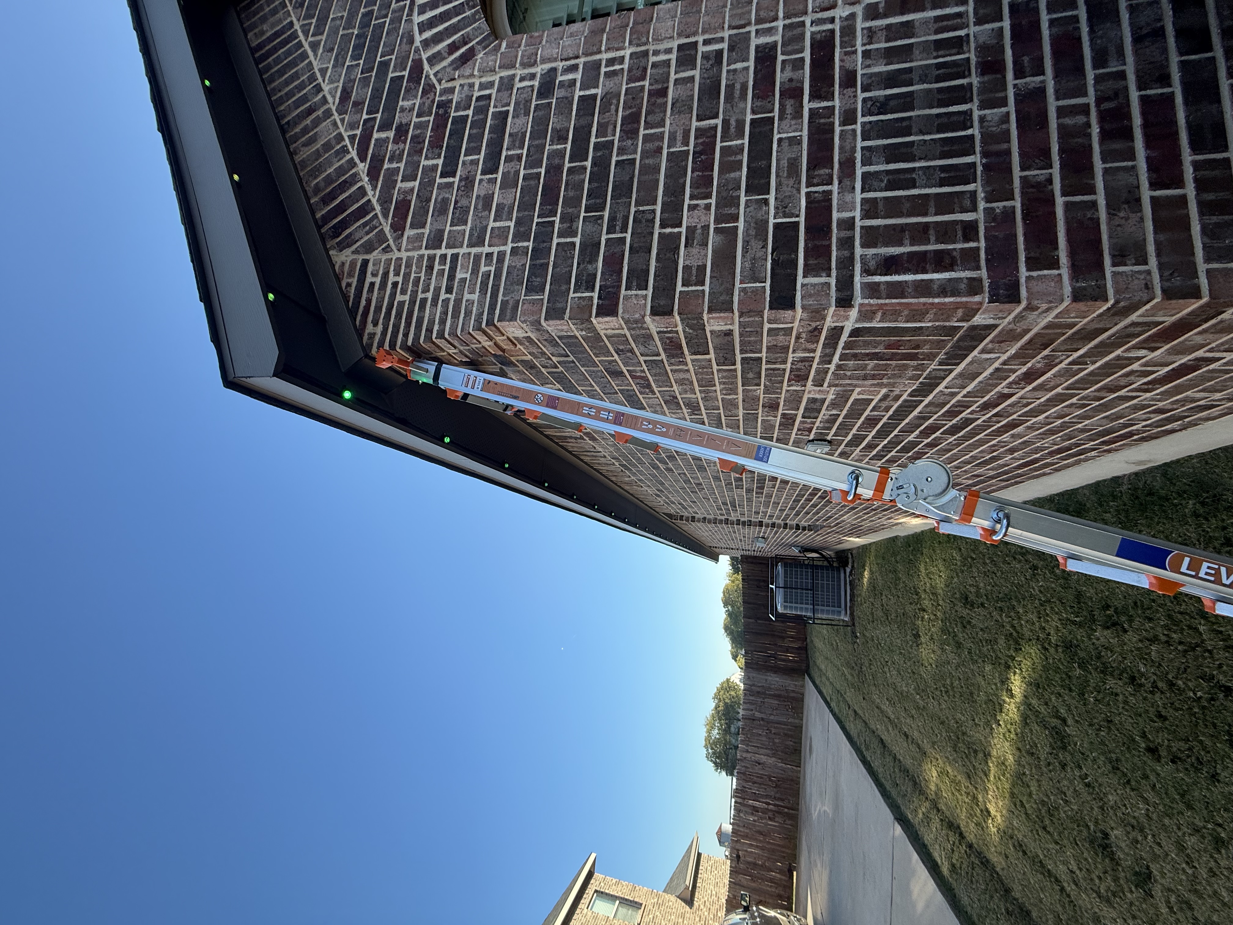 Professional installing permanent lighting on roofline with ladder